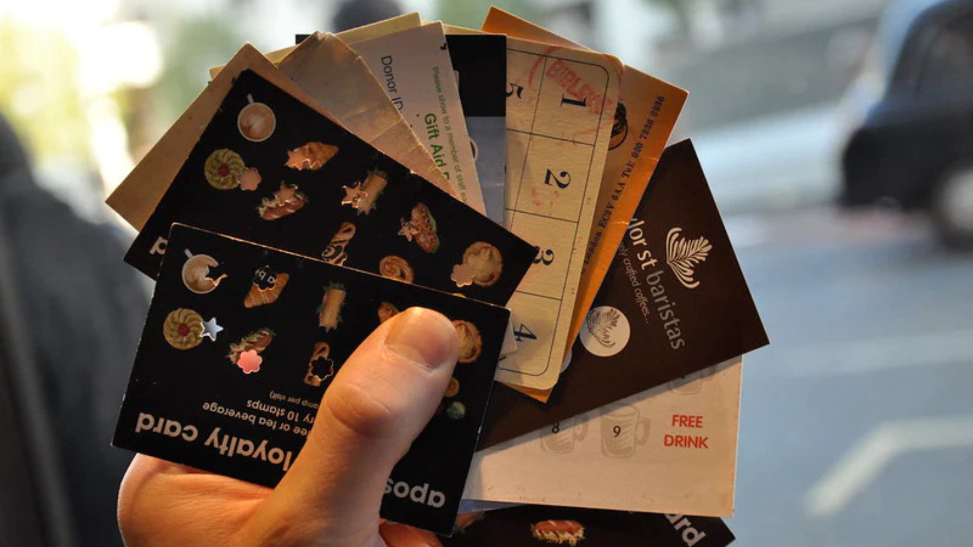 Cliente segurando vários cartões de fidelidade de papel, representando a confusão e o incômodo de lidar com programas tradicionais não digitais